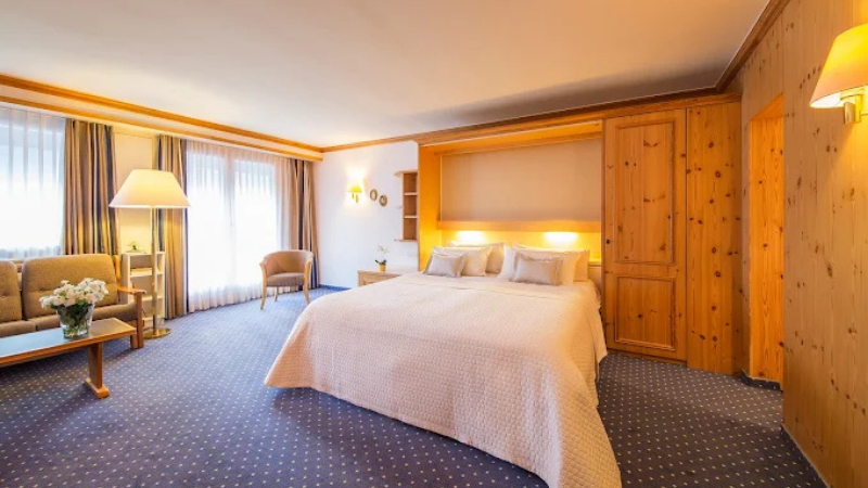 Rymligt dubbelrum på Hotel Europa med stor säng, sittgrupp, ljusa gardiner och träpaneler i klassisk alpin stil.